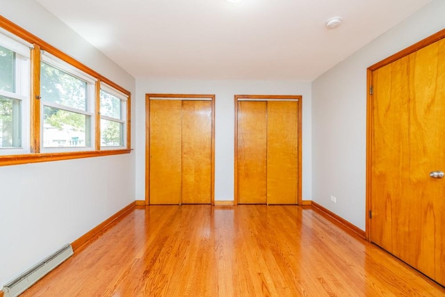 unfurnished bedroom with baseboards, baseboard heating, two closets, and light wood-type flooring