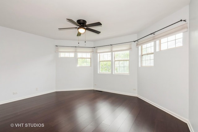 spare room featuring a ceiling fan, baseboards, dark wood-style floors, and plenty of natural light
