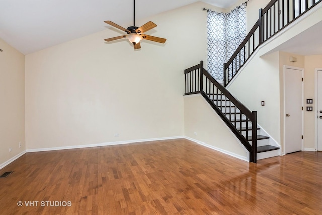 unfurnished living room featuring stairway, high vaulted ceiling, ceiling fan, and wood finished floors