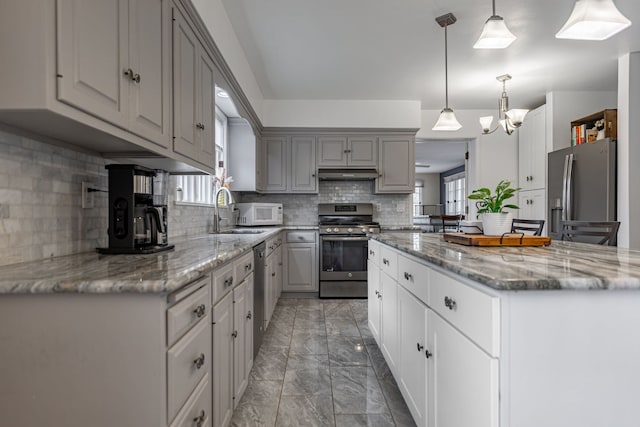 kitchen with under cabinet range hood, marble finish floor, a wealth of natural light, and appliances with stainless steel finishes