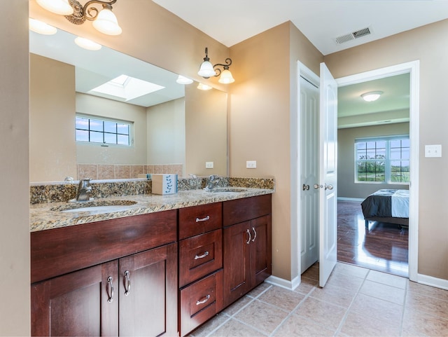 full bathroom featuring a skylight, double vanity, tile patterned flooring, baseboards, and ensuite bath