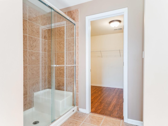 bathroom with a stall shower, a walk in closet, and wood finished floors