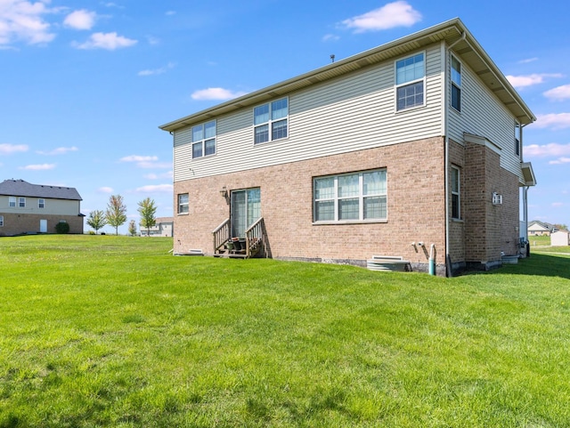 rear view of property with brick siding, a yard, and entry steps