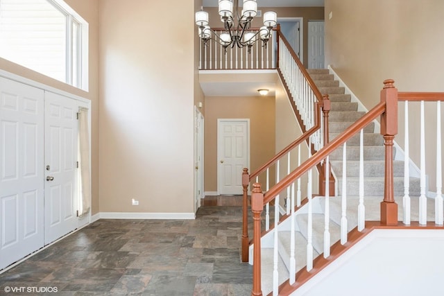 entryway featuring a chandelier, stone finish floors, baseboards, stairs, and a high ceiling