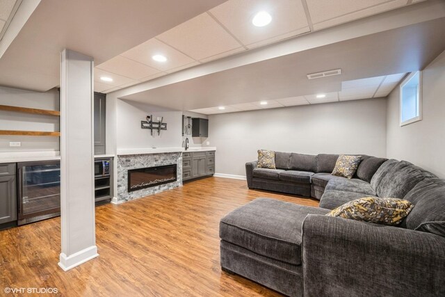 living area with light wood finished floors, bar, wine cooler, a drop ceiling, and baseboards