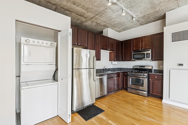 kitchen with stacked washer and clothes dryer, light wood-style flooring, dark stone counters, and appliances with stainless steel finishes