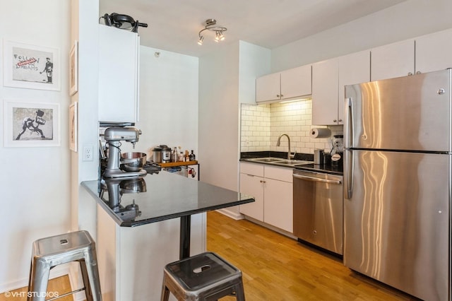 kitchen featuring light wood-style flooring, a sink, dark countertops, backsplash, and appliances with stainless steel finishes