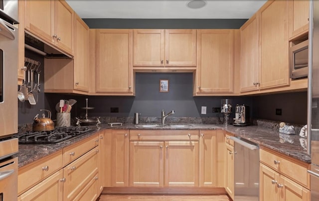 kitchen with light brown cabinets, a sink, gas stovetop, and dark stone countertops