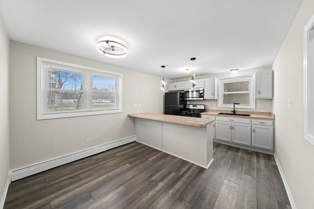 kitchen featuring a baseboard heating unit, a peninsula, dark wood-style floors, stainless steel appliances, and a sink