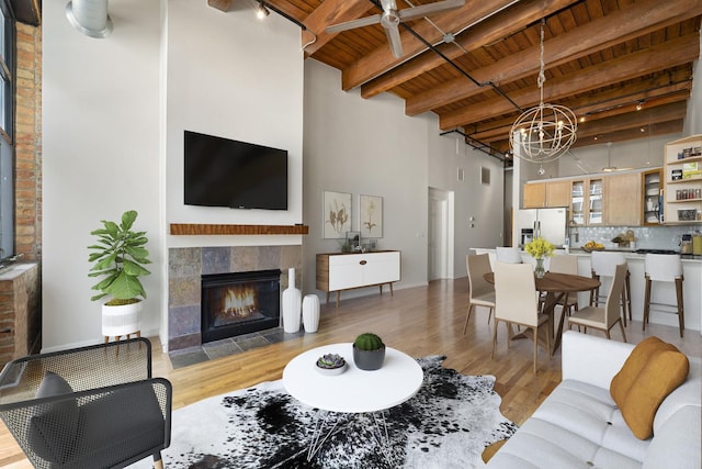 living room with light wood-type flooring, a high ceiling, beam ceiling, a tile fireplace, and wooden ceiling