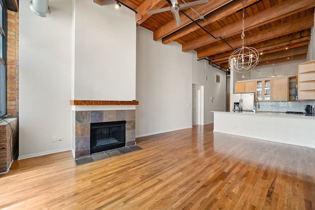 unfurnished living room featuring a tiled fireplace, beam ceiling, light wood-type flooring, and wood ceiling