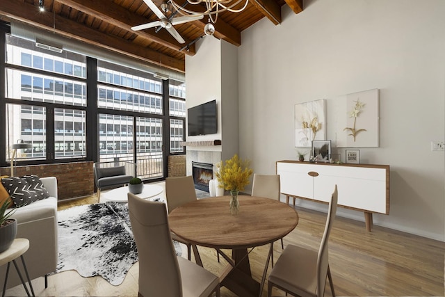 dining space featuring a tiled fireplace, beam ceiling, wooden ceiling, and wood finished floors