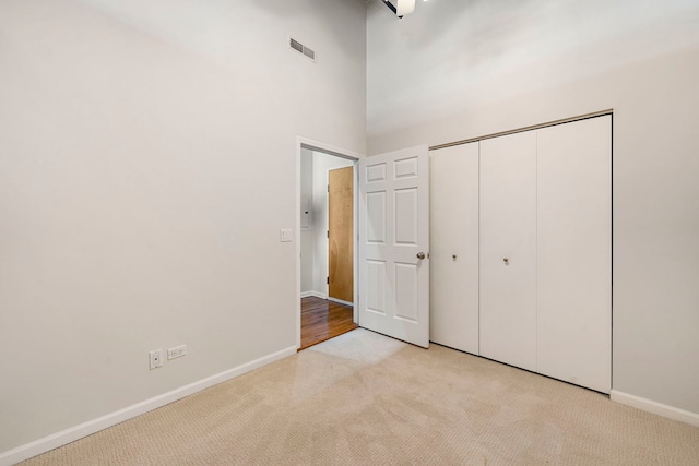 unfurnished bedroom with a towering ceiling, baseboards, a closet, light carpet, and visible vents