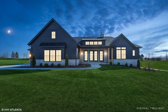 view of front of home featuring a standing seam roof, metal roof, a front yard, stone siding, and a chimney