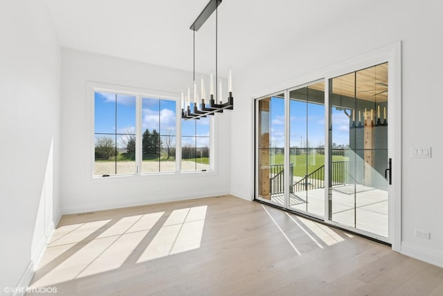 unfurnished dining area featuring wood finished floors, a notable chandelier, and baseboards
