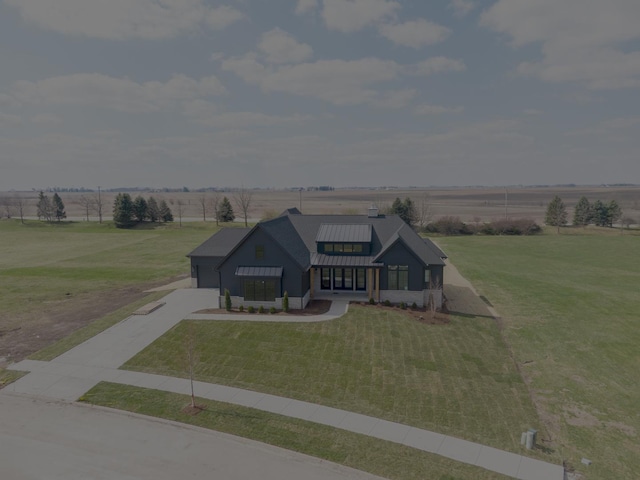 view of front facade with a standing seam roof, a rural view, metal roof, a front lawn, and concrete driveway