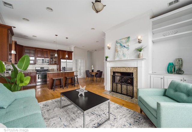 living area with crown molding, light wood-style flooring, a fireplace with flush hearth, and recessed lighting