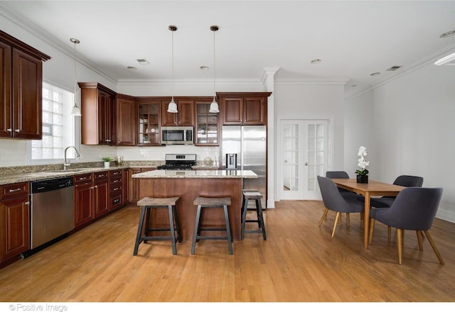 kitchen with appliances with stainless steel finishes, light wood-style flooring, a breakfast bar area, backsplash, and ornamental molding