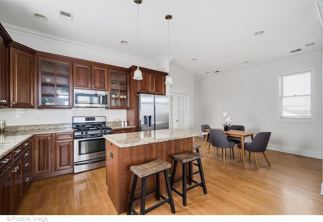kitchen featuring stainless steel appliances, light wood-style floors, a center island, ornamental molding, and decorative backsplash