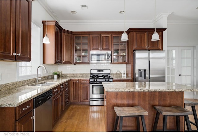 kitchen featuring appliances with stainless steel finishes, a sink, a breakfast bar, light wood-style flooring, and glass insert cabinets