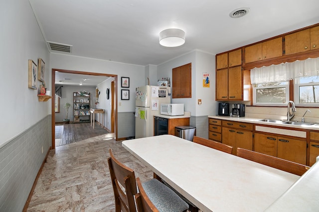 kitchen featuring brown cabinetry, visible vents, a sink, and white appliances