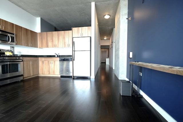 kitchen featuring baseboards, modern cabinets, dark wood-style flooring, appliances with stainless steel finishes, and dark countertops