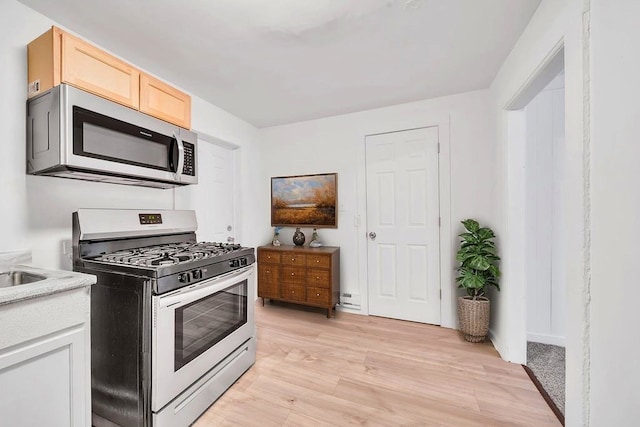 kitchen with appliances with stainless steel finishes, light wood-type flooring, light countertops, baseboards, and light brown cabinets