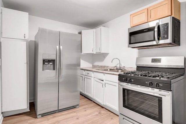 kitchen with appliances with stainless steel finishes, a sink, light countertops, white cabinets, and light wood-style floors