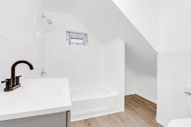 full bath with vanity, wood finished floors, toilet, shower / bath combination, and vaulted ceiling