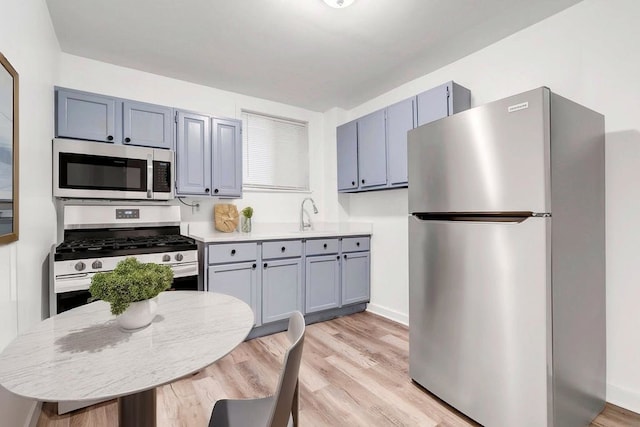 kitchen featuring appliances with stainless steel finishes, a sink, light countertops, gray cabinets, and light wood-type flooring