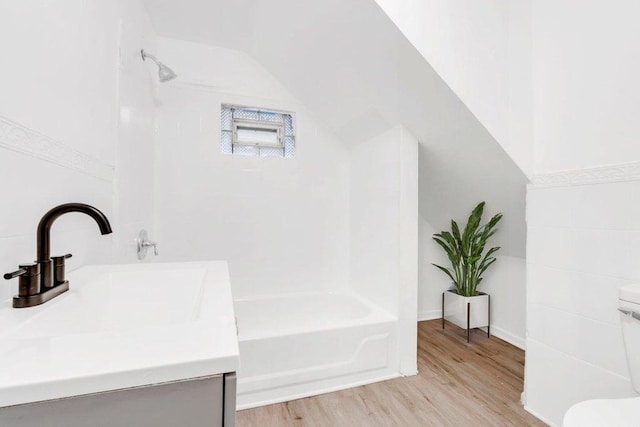 bathroom with vaulted ceiling, shower / tub combination, wood finished floors, vanity, and toilet