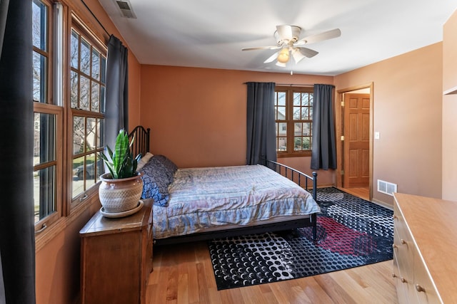 bedroom with ceiling fan, visible vents, baseboards, and wood finished floors