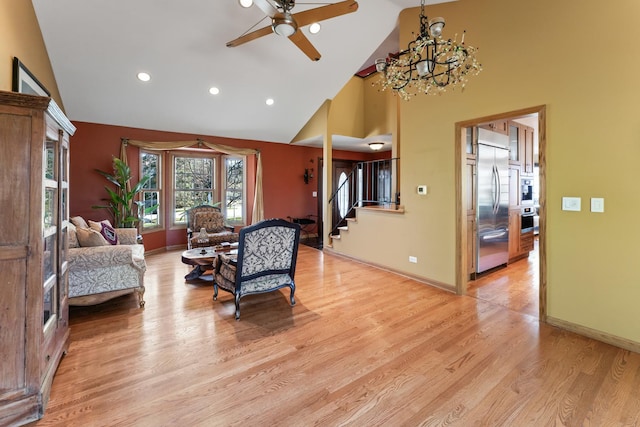 living area with ceiling fan with notable chandelier, high vaulted ceiling, recessed lighting, stairs, and light wood finished floors