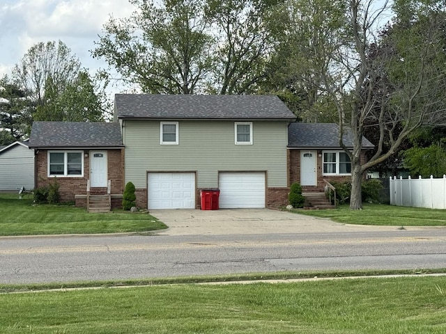 split level home featuring fence, a front yard, brick siding, an attached garage, and driveway