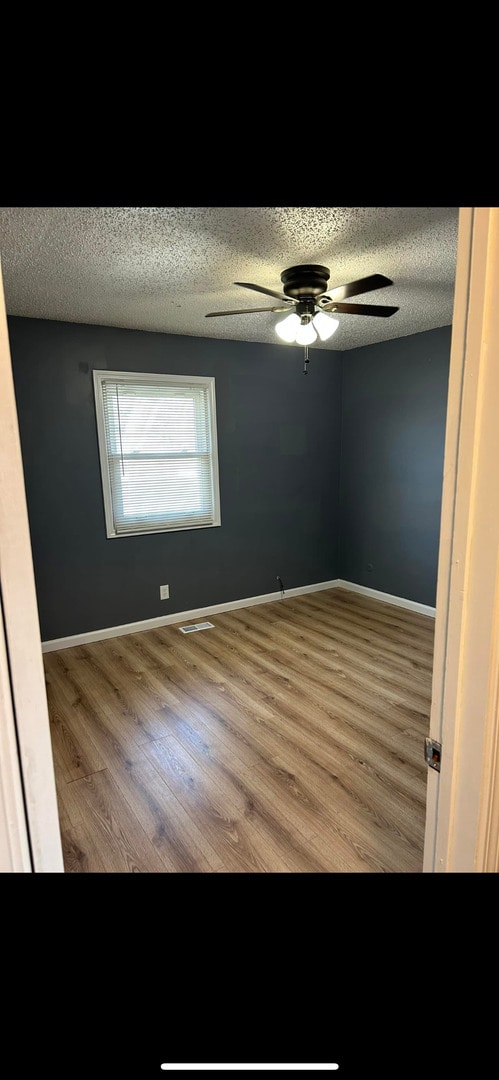 empty room with baseboards, a ceiling fan, a textured ceiling, and wood finished floors