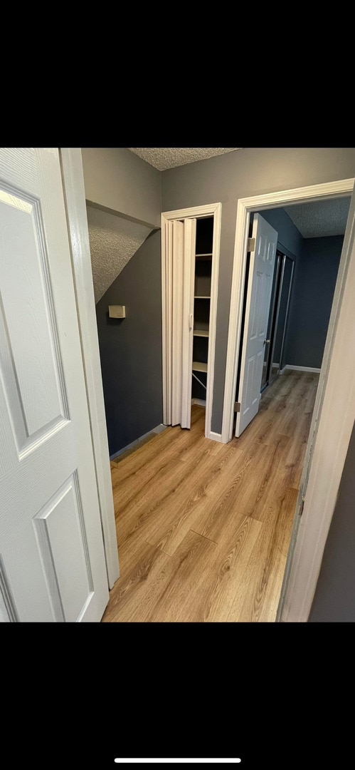 corridor featuring baseboards, a textured ceiling, and light wood finished floors