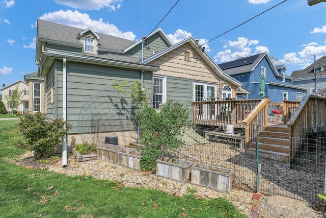 rear view of house featuring roof with shingles, a wooden deck, and a vegetable garden