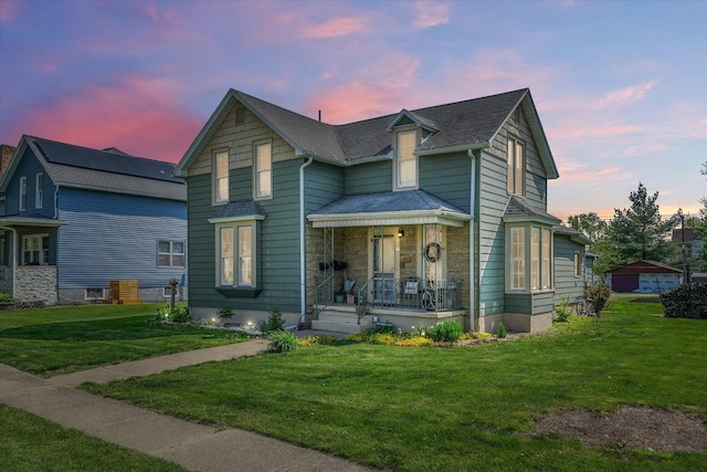 view of front facade featuring a porch, a shingled roof, and a front lawn