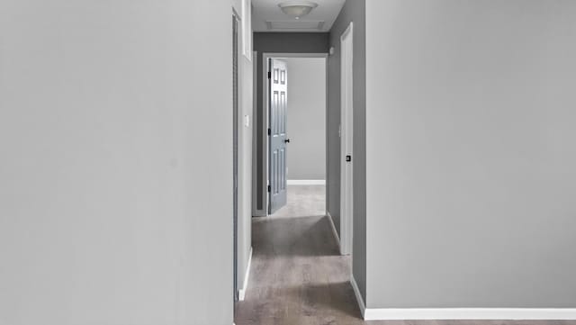 hallway with baseboards, attic access, and wood finished floors