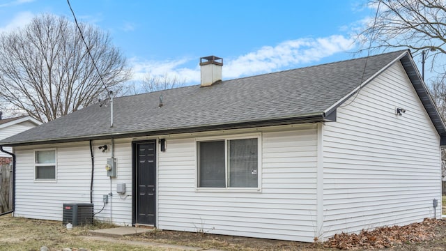 back of house with central air condition unit, roof with shingles, and a chimney