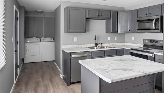 kitchen with gray cabinets, wood finished floors, washing machine and clothes dryer, a sink, and stainless steel appliances