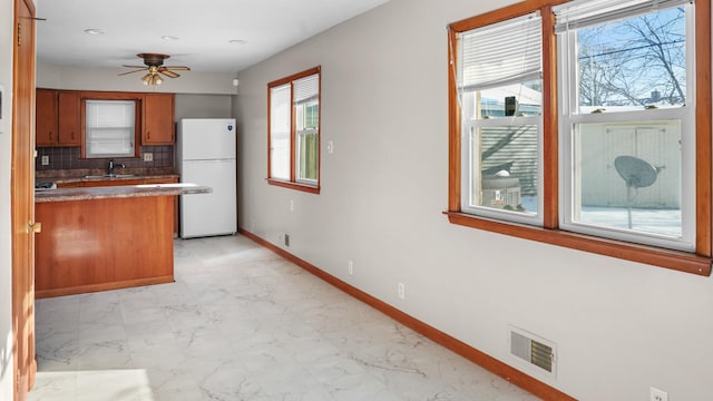 kitchen featuring baseboards, freestanding refrigerator, backsplash, visible vents, and brown cabinetry