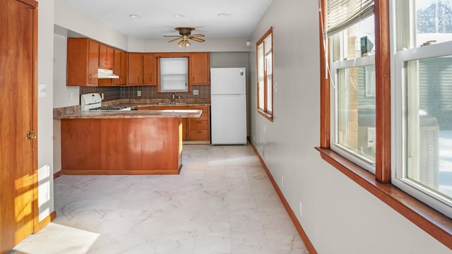 kitchen with a sink, brown cabinetry, white appliances, and baseboards