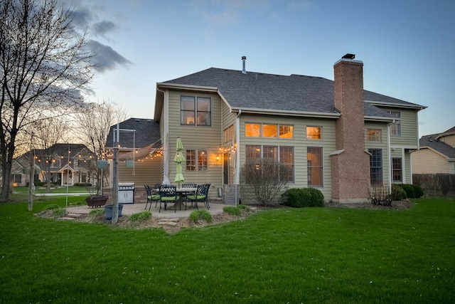 back of house featuring a lawn, roof with shingles, a chimney, and a patio area