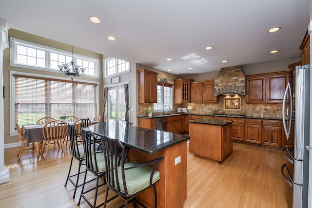 kitchen featuring brown cabinetry, a center island, custom range hood, a sink, and stainless steel appliances