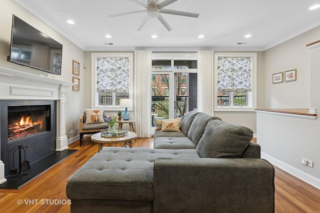 living room featuring a ceiling fan, a warm lit fireplace, wood finished floors, baseboards, and recessed lighting