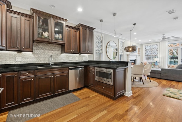 kitchen featuring a sink, stainless steel appliances, open floor plan, a lit fireplace, and dark brown cabinets