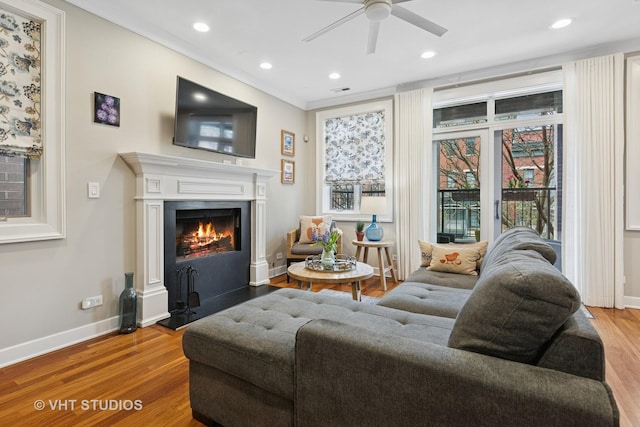 living area with a ceiling fan, wood finished floors, a warm lit fireplace, baseboards, and recessed lighting