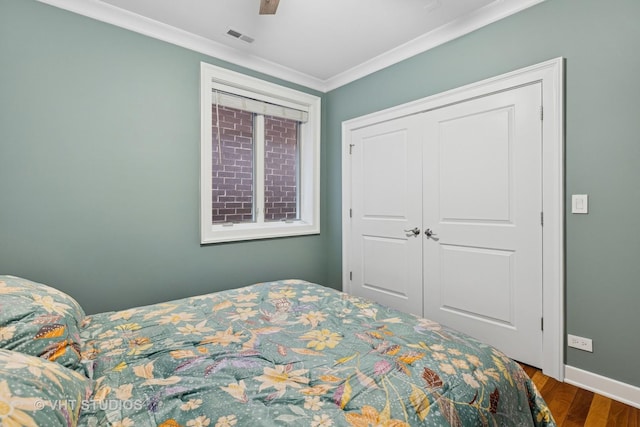 bedroom with ornamental molding, wood finished floors, baseboards, and a closet