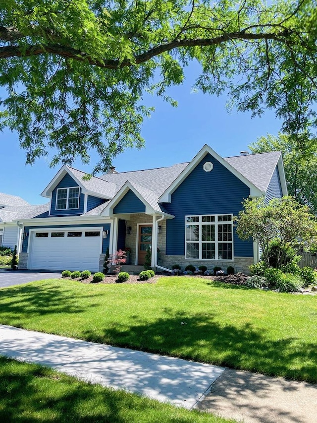 craftsman inspired home featuring driveway, a front yard, an attached garage, a shingled roof, and stone siding